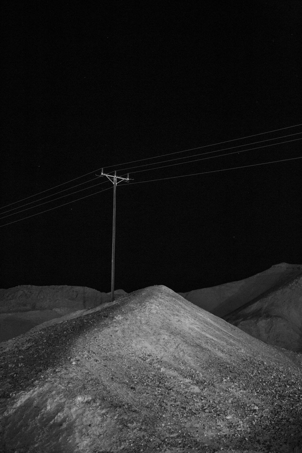 Ein einsamer Strommast steht in einer kargen Landschaft unter einem dunklen Nachthimmel und fängt die raue Schönheit ein, die ein Werbefotograf aus Nürnberg oft sucht.