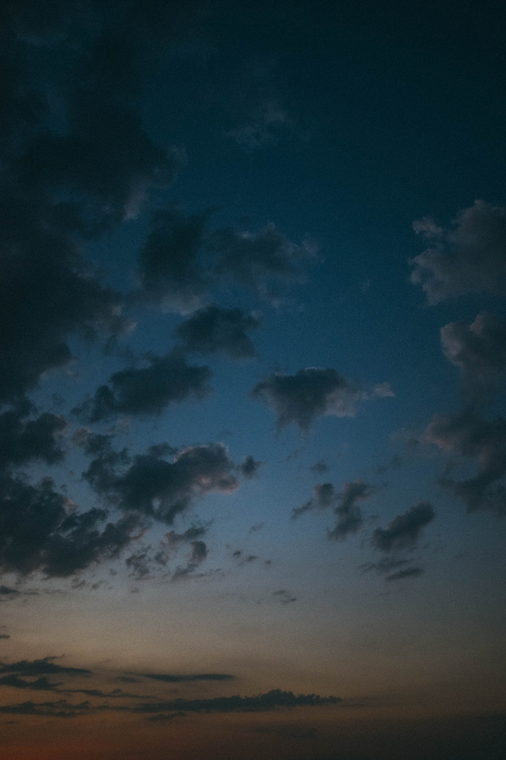 Ein heiterer Himmel mit vereinzelten Wolken in der Dämmerung, der einen Farbverlauf von Dunkelblau zu einem Hauch von Orange in der Nähe des Horizonts zeigt – ein idealer Hintergrund für jede kommerzielle Aufnahme, perfekt für Businessfotografie.