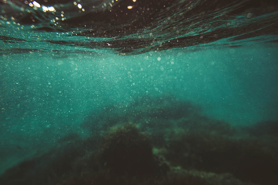 Unterwasseransicht mit verschwommenem Blick auf die Meeresoberfläche oben und undeutlichen Merkmalen des Meeresbodens darunter. Eine Szene wie der Traum eines Sportfotografen, in der Bewegung und Geheimnis verschmelzen.