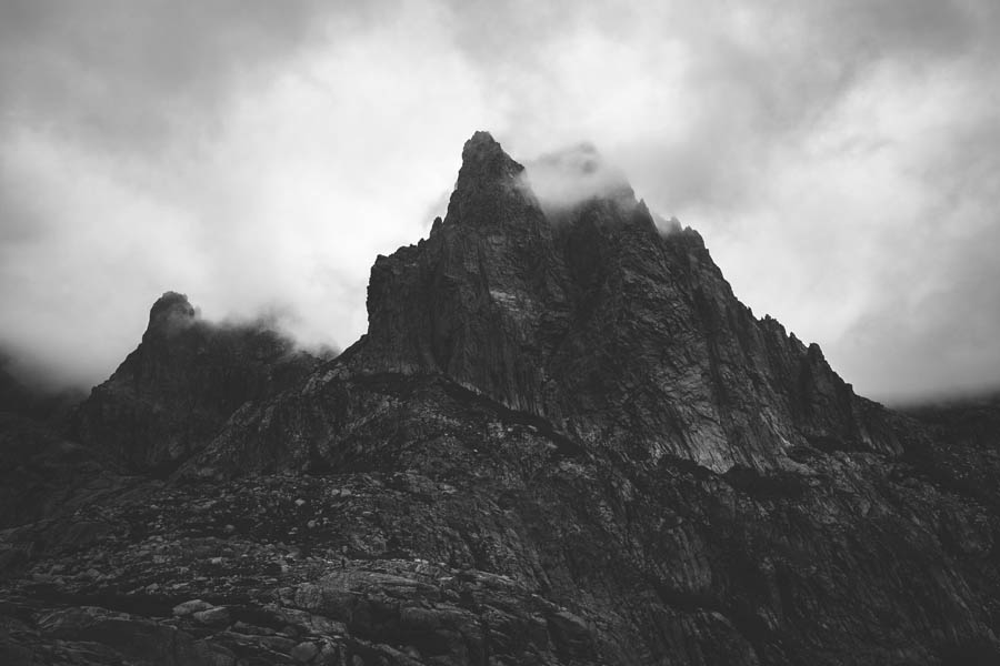 Ein dramatisches Schwarzweißfoto eines Werbefotografen aus Nürnberg, das schroffe, teilweise von Wolken verdeckte Berggipfel zeigt, weckt ein intensives Gefühl von Abenteuer.