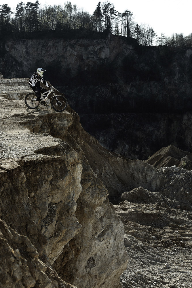 Ein Mountainbiker steht am Rand einer steilen Felsklippe und bereitet sich auf den Abstieg in eine raue Landschaft vor. Ein Werbefotograf aus Nürnberg hat dies in seinem hochmodernen Fotostudio für eine bevorstehende Kampagne perfekt eingefangen.